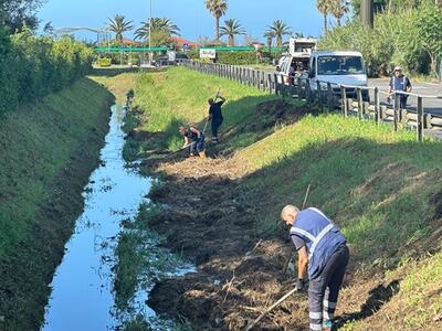 Due operai mandati dal Consorzio per pulire l'enormità di sfalci lasciati sugli argini dei fiumi versiliesi: lo sconcerto di Emanuele Ricciardi, costretto da anni a pulire le montagne di sfalci che ostruiscono la sua darsena